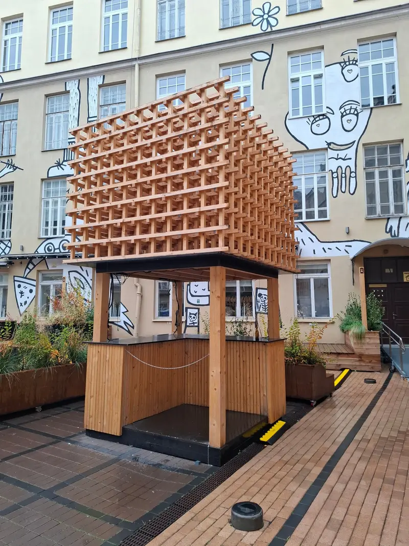 Kioskas su medinių grotelių konstrukcija ant stogo ir lentelėmis apkaltu prekystaliu
